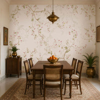 Blossom Veil Mural – Dusty Rose Pink floral wallpaper displayed across an elegant Indian-inspired dining room, featuring delicate pastel pink and peach blossoms intertwined with warm ivory vines, soft botanical branches, muted green leaves, and fine floral detailing on a subtle dusty rose pink background. The graceful floral composition flows seamlessly across the feature wall, creating a refined and sophisticated look. The room includes a traditional wooden dining table with woven 
