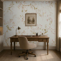 "A cozy home office with a wooden desk, beige swivel chair, brass desk lamp, and books neatly arranged. A framed landscape artwork hangs above the desk against light floral wallpaper. Built-in shelves with books and decor sit to the left, while a window on the right brings in natural light. A neutral rug covers the floor, complementing the warm and elegant aesthetic."  