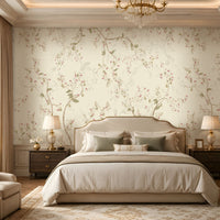 Warm ivory cream floral wallpaper with delicate botanical branches, soft pink flowers, muted sage green leaves, and subtle beige accents covering a large feature wall in an elegant luxury bedroom. The sophisticated room features a cream upholstered bed, neutral bedding, dark wooden bedside tables, classic lamps, a crystal chandelier, arched window with beige curtains, plush seating, decorative furniture, and a warm refined interior that complements the wallpaper’s soft botanical design.
