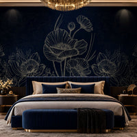 A luxury bedroom featuring a dark navy blue floral wallpaper with white poppy line art, a matching navy velvet bed with beige and blue pillows, a navy velvet bench with gold trim, and a gold chandelier overhead.