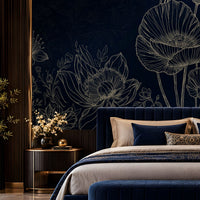 A luxury bedroom featuring a dark navy blue floral wallpaper with white poppy line art, a matching navy velvet bed with beige and blue pillows, a navy velvet bench with gold trim, and a gold chandelier overhead.