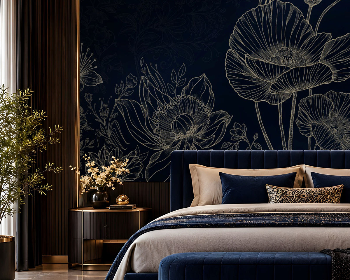 A luxury bedroom featuring a dark navy blue floral wallpaper with white poppy line art, a matching navy velvet bed with beige and blue pillows, a navy velvet bench with gold trim, and a gold chandelier overhead.