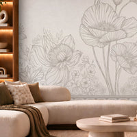 A modern living room featuring a large wall mural with delicate gray floral line art on a light beige background. The room is styled with a cream-colored sectional sofa, a round stone coffee table, a wooden armchair, and warm ambient lighting.