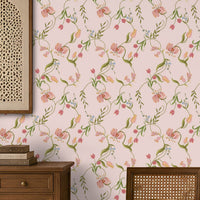 A dining room interior featuring a light pink floral wallpaper as the main wall backdrop, with a wooden dining table and woven-back chairs placed in front of it. A hanging lantern, sideboard, and decorative wall art are also visible. 