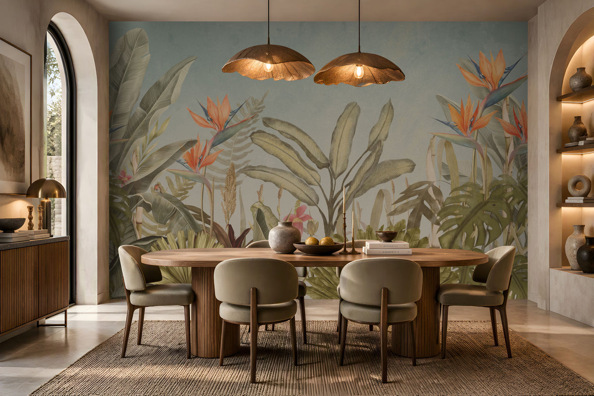Earthy Tropical Oasis - Dusty Blue botanical wallpaper featuring lush tropical foliage, oversized bird-of-paradise flowers in warm orange, coral, and muted blue tones, and layered olive green leaves against a soft dusty blue background. Showcased in an elegant dining room with a natural wooden dining table, upholstered chairs in earthy neutral shades, warm pendant lighting, and textured décor, this tropical wallpaper brings a calming, nature-inspired charm and sophisticated elegance to contemporar