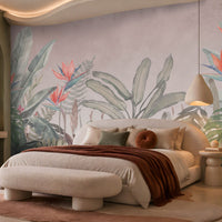 Earthy Tropical Oasis - Dusty Mauve Pink botanical wallpaper featuring oversized tropical foliage, elegant bird-of-paradise flowers in coral pink and muted blue, and layered olive green leaves against a soft dusty mauve pink background. Showcased in a luxurious bedroom with a curved cream upholstered bed, earthy terracotta accents, plush neutral bedding, and warm ambient lighting, this elegant tropical wallpaper combines delicate pink undertones with natural botanical elements to create a serene