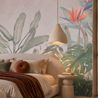 Earthy Tropical Oasis - Dusty Mauve Pink botanical wallpaper featuring oversized tropical foliage, elegant bird-of-paradise flowers in coral pink and muted blue, and layered olive green leaves against a soft dusty mauve pink background. Showcased in a luxurious bedroom with a curved cream upholstered bed, earthy terracotta accents, plush neutral bedding, and warm ambient lighting, this elegant tropical wallpaper combines delicate pink undertones with natural botanical elements to create a serene