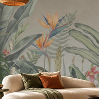 Earthy Tropical Oasis - Olive Green botanical wallpaper featuring lush tropical leaves, oversized bird-of-paradise flowers in golden yellow, orange, and muted blue, and delicate pink floral accents against a warm beige background. Displayed in a spacious, elegant living room with a curved cream sofa, natural wood furniture, woven textures, and earthy decorative elements, this nature-inspired wallpaper creates a serene tropical atmosphere with sophisticated olive green tones.
