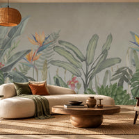Earthy Tropical Oasis - Olive Green botanical wallpaper featuring lush tropical leaves, oversized bird-of-paradise flowers in golden yellow, orange, and muted blue, and delicate pink floral accents against a warm beige background. Displayed in a spacious, elegant living room with a curved cream sofa, natural wood furniture, woven textures, and earthy decorative elements, this nature-inspired wallpaper creates a serene tropical atmosphere with sophisticated olive green tones.