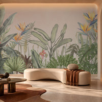 Earthy Tropical Oasis - Warm Ivory Pink botanical wallpaper featuring lush tropical leaves, elegant bird-of-paradise flowers in soft yellow, orange, and muted blue, and layered olive green foliage against a warm ivory pink background. Displayed in a sophisticated contemporary lounge with a sculptural cream sofa, natural stone finishes, a dark wooden coffee table, and warm ambient lighting, this elegant tropical wallpaper adds a soft, earthy charm and a serene, nature-inspired atmosphere to modern 
