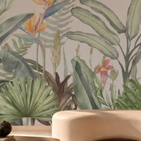 Earthy Tropical Oasis - Warm Ivory Pink botanical wallpaper featuring lush tropical leaves, elegant bird-of-paradise flowers in soft yellow, orange, and muted blue, and layered olive green foliage against a warm ivory pink background. Displayed in a sophisticated contemporary lounge with a sculptural cream sofa, natural stone finishes, a dark wooden coffee table, and warm ambient lighting, this elegant tropical wallpaper adds a soft, earthy charm and a serene, nature-inspired atmosphere to modern 