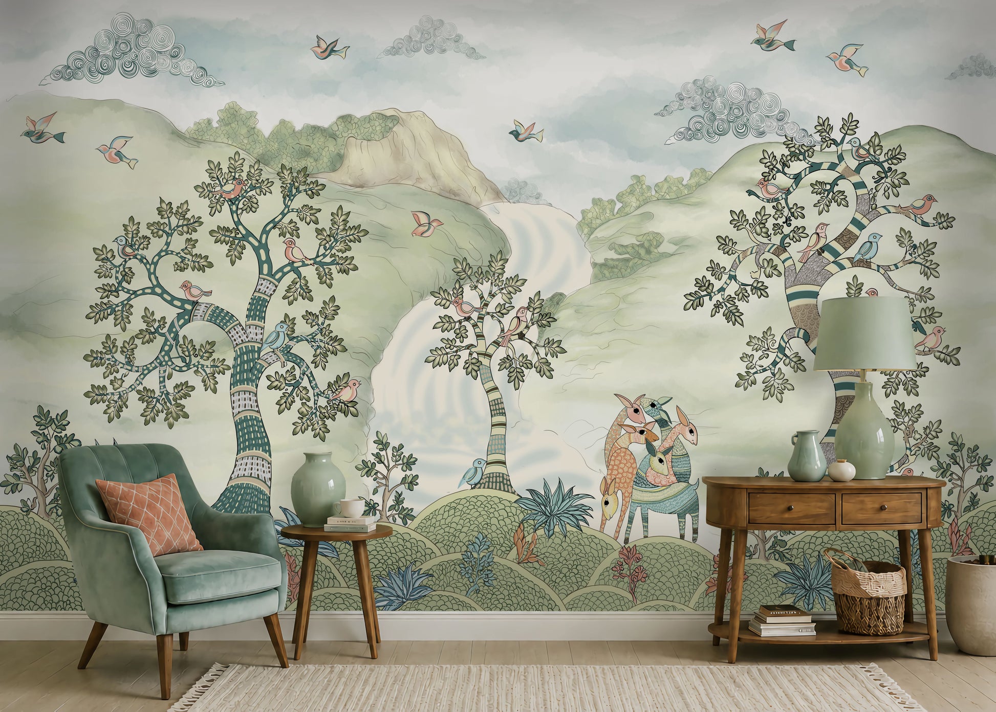 Pastel woodland wall mural featuring hand-painted sage green trees, birds in flight, and deer in a serene forest landscape, styled in a cozy living room with a green armchair and wooden console table.