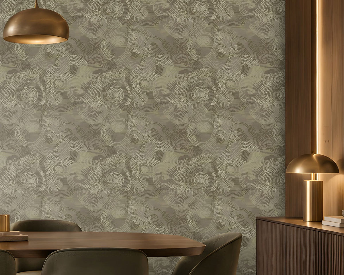 A spacious modern dining room featuring a large accent wall decorated with seamless floral swirl wallpaper in muted olive grey, soft sage, and warm taupe tones. The intricate repeating floral pattern adds depth, texture, and understated elegance to the interior. A rich dark wooden dining table paired with plush olive grey upholstered chairs complements the wallpaper beautifully, while elegant brass pendant lights, warm wooden cabinetry, and soft ambient lighting create a sophisticated atmosphere.
