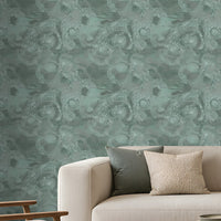 Modern minimalist living room featuring a calming teal and natural wood color palette. A large statement wall covered in textured teal wallpaper with an intricate swirling pattern forms the backdrop to the space. Positioned in front of the wall is a cream-colored sofa accented with soft green and ivory cushions, with a matching teal throw blanket draped over the right armrest.
