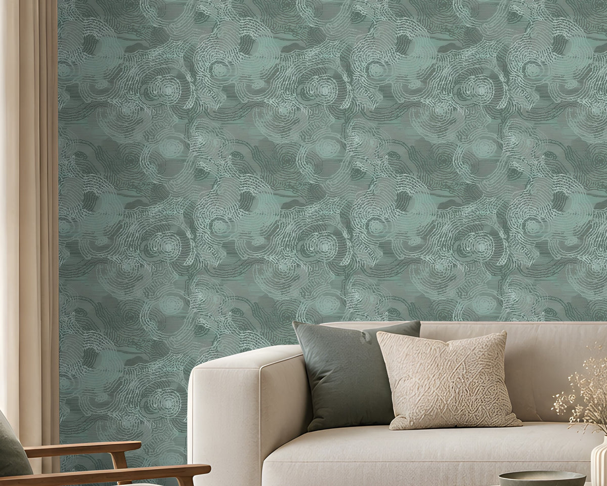 Modern minimalist living room featuring a calming teal and natural wood color palette. A large statement wall covered in textured teal wallpaper with an intricate swirling pattern forms the backdrop to the space. Positioned in front of the wall is a cream-colored sofa accented with soft green and ivory cushions, with a matching teal throw blanket draped over the right armrest.