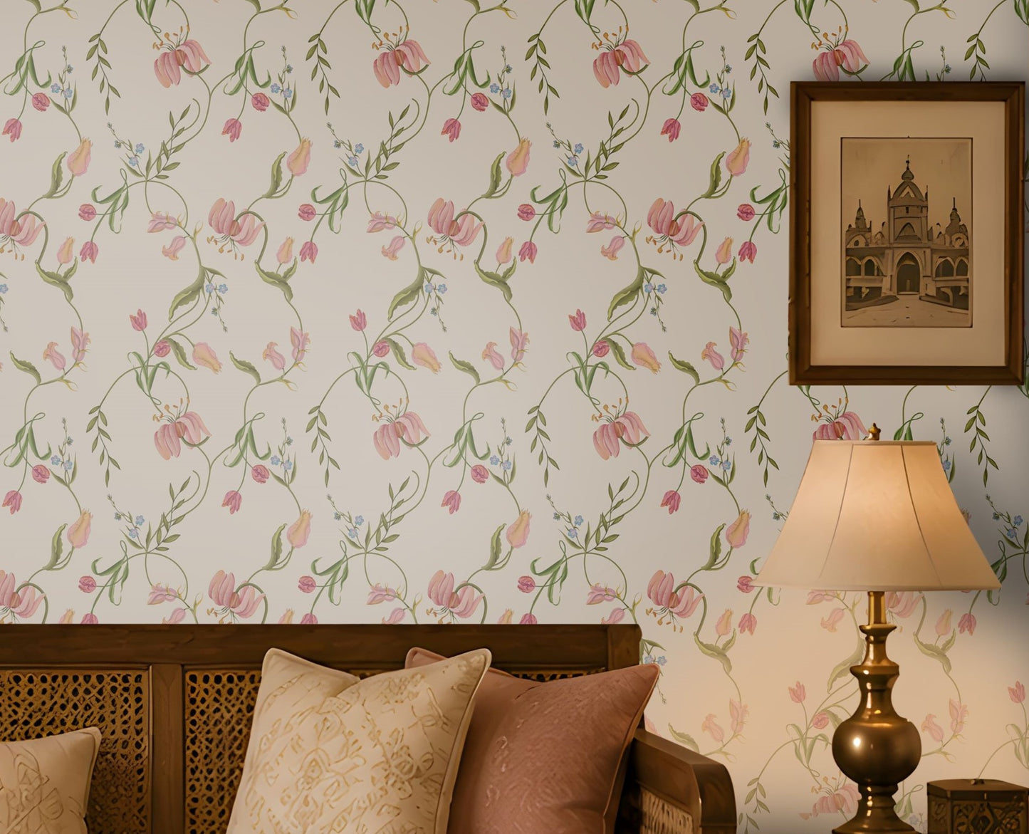 A warm and elegant living room featuring soft pink floral wallpaper with delicate green vines and blossoms. A wooden daybed-style sofa with a cane back and cream upholstery is accented with blush pink and beige cushions. Matching wooden side tables hold a decorative lantern and a table lamp, while a simple coffee table with books and a decorative bowl sits on a natural woven rug. Sunlight streams through a carved wooden window, creating soft shadows and enhancing the room's cozy, traditional ambiance.