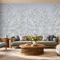 Elegant living room featuring Florentine Bloom misty blue floral wallpaper with white roses and botanical vines, complemented by a cream sofa, wooden furniture, and natural window lighting.