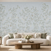 Elegant living room featuring Florentine Bloom powder blue floral wallpaper with white roses and botanical vines, complemented by a cream sofa, wooden furniture, and natural daylight.