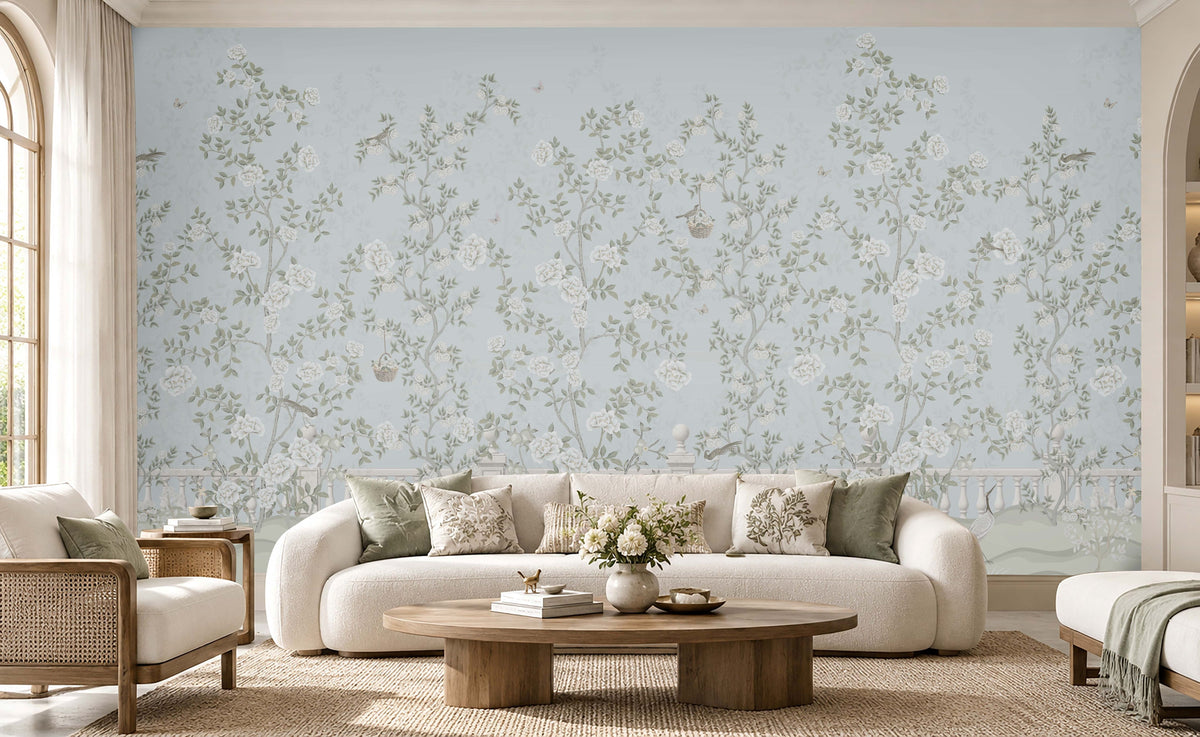 Elegant living room featuring Florentine Bloom powder blue floral wallpaper with white roses and botanical vines, complemented by a cream sofa, wooden furniture, and natural daylight.
