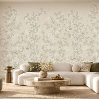 Luxury living room featuring Florentine Bloom soft beige floral wallpaper with white roses and botanical vines, complemented by a cream sofa, wooden furniture, and natural window lighting.