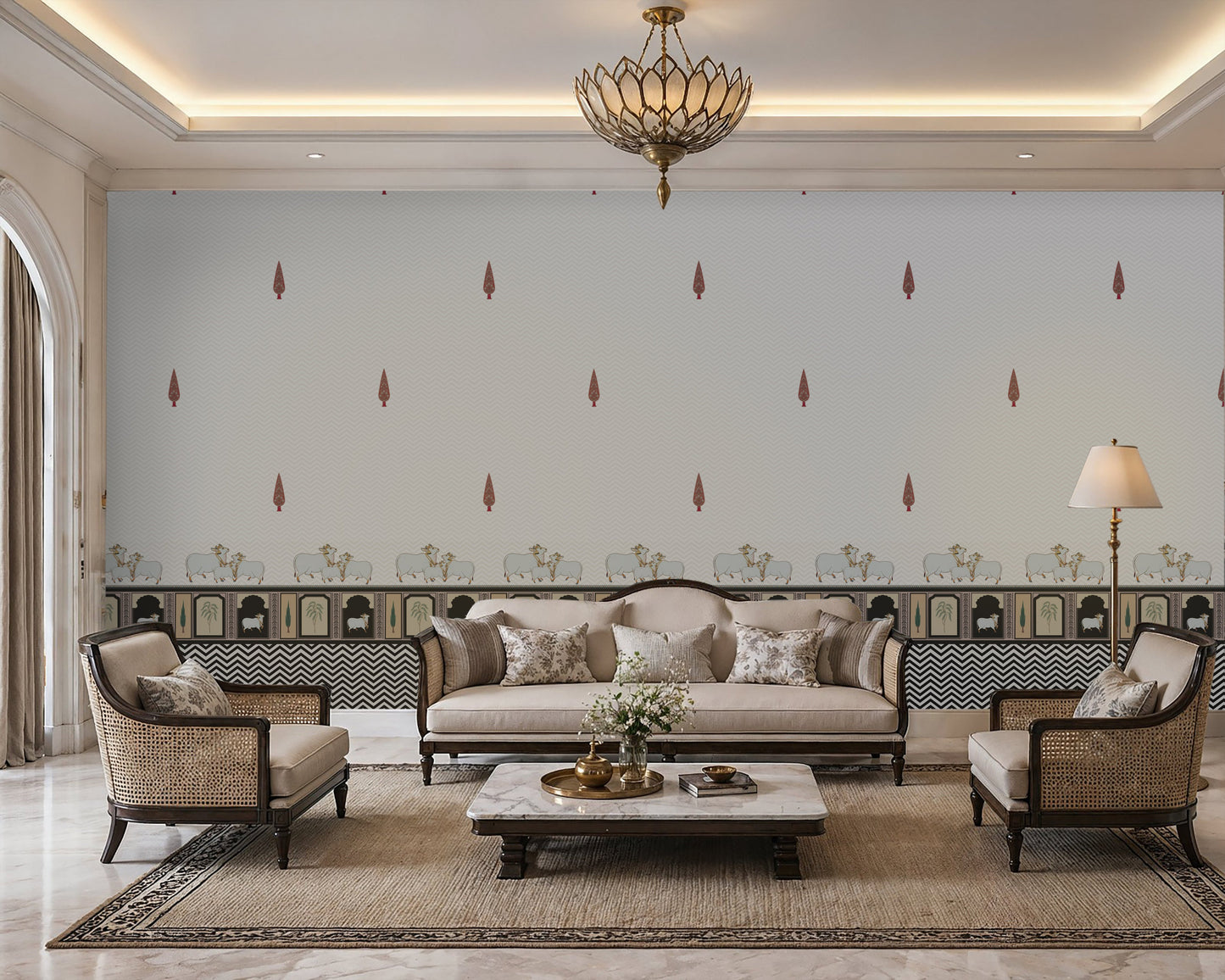 Elegant Indian living room featuring a Pichwai motif seamless wallpaper with soft grey chevron patterns, delicate red paisley accents, and traditional cow illustrations along a decorative border. The space is styled with neutral-toned premium furniture, cane armchairs, a classic sofa, brass lighting, and a marble center table, creating a soothing, luxurious Hyderabad-inspired ambience with the wallpaper clearly visible as the focal point.