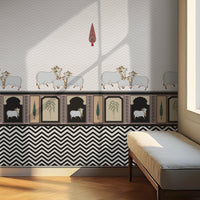 Black-and-white interior scene with a patterned wall featuring small animal motifs and geometric designs. A cushioned bench sits along the wall beside a large window letting in soft light. A hanging ceiling lamp is visible above, and sunlight casts angular shadows across the wall and wooden floor.