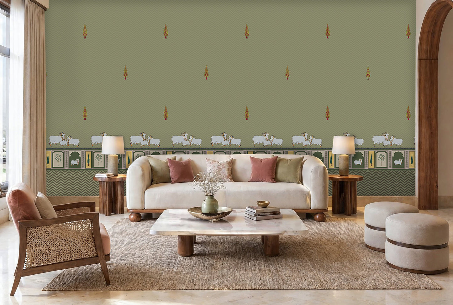 Green-toned room with patterned wallpaper featuring small decorative motifs and a horizontal border with sheep illustrations. A white vintage-style desk with curved legs sits against the wall, paired with a cushioned stool. On the desk is a patterned lamp and an open book. To the left, tall glass-paneled doors let in natural light, and the floor is tiled in a light color with small black diamond accents.