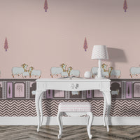 Light pink room with patterned wallpaper featuring small decorative motifs and sheep illustrations along a border. A white vintage-style desk with curved legs sits against the wall, paired with a small cushioned stool. On the desk is a white lamp with a patterned shade and a small decorative object. The floor has a textured, zigzag-patterned rug in neutral tones.