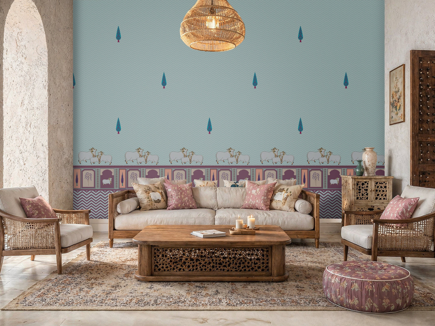 An elegantly decorated living room featuring a large accent wall with light blue wallpaper. The wallpaper is adorned with a pattern of small, stylized teal cypress trees and a decorative border along the bottom showing white cows and traditional arch motifs in purple and pink.