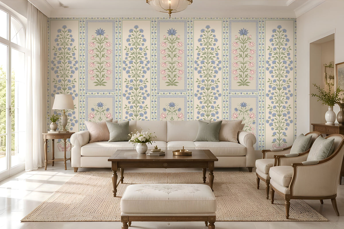 Elegant contemporary living room featuring blue, pastel pink, and muted sage green floral wallpaper with intricate botanical motifs and decorative panel borders on a warm ivory background. The heritage-inspired wallpaper creates a sophisticated focal wall, complemented by a cream upholstered sofa, matching accent armchairs, neutral cushions, a dark wooden coffee table, and a textured beige rug.