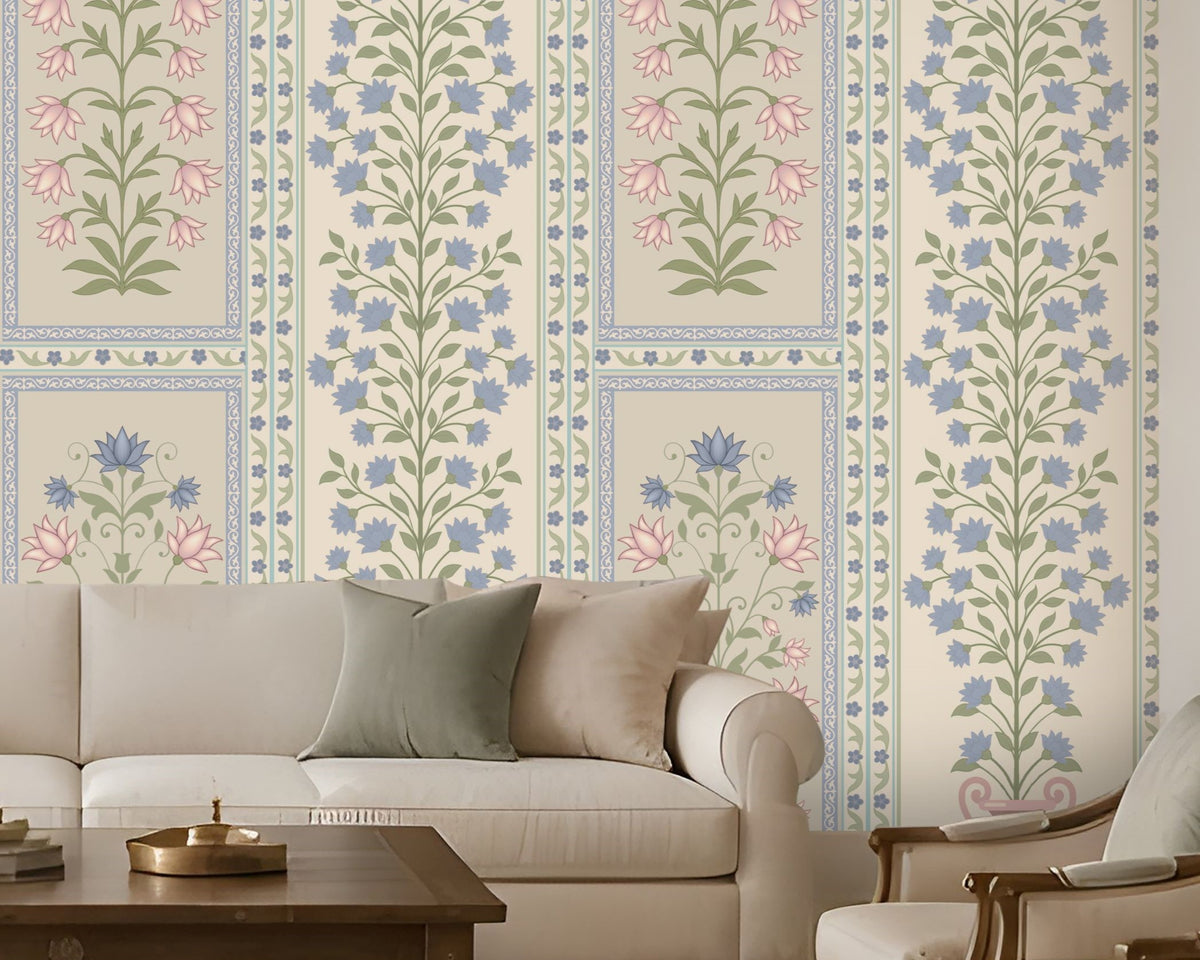 Elegant contemporary living room featuring blue, pastel pink, and muted sage green floral wallpaper with intricate botanical motifs and decorative panel borders on a warm ivory background. The heritage-inspired wallpaper creates a sophisticated focal wall, complemented by a cream upholstered sofa, matching accent armchairs, neutral cushions, a dark wooden coffee table, and a textured beige rug.