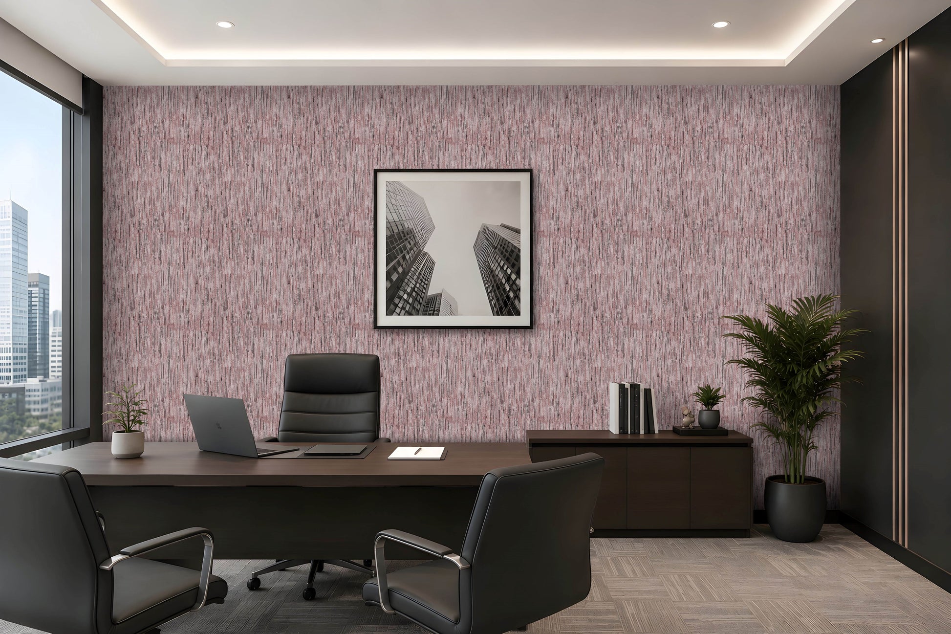 A modern office interior featuring textured pink wallpaper on the main wall, a dark wood conference table, black office chairs, a laptop, a framed black-and-white cityscape print, and a potted plant.