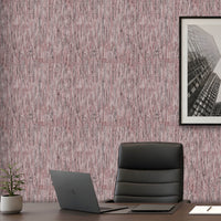A styled office interior featuring textured wallpaper with a vertical brushstroke pattern in dusty pink, mauve, and gray. A dark gray leather office chair sits on a dark wood desk next to an open laptop, with a small potted plant and a framed black-and-white cityscape print on the wall.