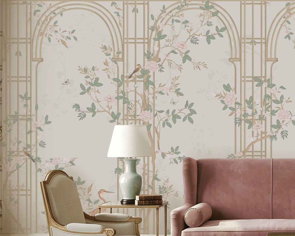 Morning Dew Trellis wallpaper in warm ivory and champagne tones featuring elegant trellis arches, delicate flowering vines, perched birds, butterflies, and soft botanical details. Styled in a sophisticated living room with a blush velvet sofa, classic armchairs, decorative table lamps, a green marble coffee table, and ornate architectural moldings, the mural creates a refined garden-inspired backdrop with timeless elegance and luxurious charm.