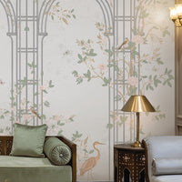 Morning Dew Trellis wallpaper featured in a luxurious living room, showcasing elegant powder blue trellis arches intertwined with delicate floral vines, blooming branches, birds, and botanical motifs. Surrounded by intricately carved wall panels, crystal chandeliers, plush seating, brass accents, and soft lighting, the mural creates a refined blend of classic elegance, garden-inspired beauty, and timeless sophistication.