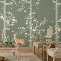 Morning Dew Trellis wallpaper in deep sage green featuring elegant arched trellis detailing, delicate flowering branches, perched birds, butterflies, and graceful woodland animals. Displayed in a luxurious living room with a coffered wood ceiling, crystal chandelier, blush-toned chaise lounge, vintage armchairs, and warm wood flooring, the mural creates a sophisticated garden-inspired focal point that blends classic elegance with nature-inspired charm.