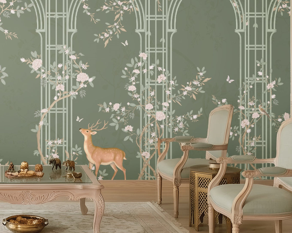 Morning Dew Trellis wallpaper in deep sage green featuring elegant arched trellis detailing, delicate flowering branches, perched birds, butterflies, and graceful woodland animals. Displayed in a luxurious living room with a coffered wood ceiling, crystal chandelier, blush-toned chaise lounge, vintage armchairs, and warm wood flooring, the mural creates a sophisticated garden-inspired focal point that blends classic elegance with nature-inspired charm.