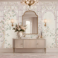 Morning Dew Trellis wallpaper in soft blush pink featuring elegant trellis arches, delicate flowering branches, perched birds, butterflies, and graceful botanical details. Styled in a sophisticated entryway with a curved gold-framed mirror, floral chandelier, fluted console table, decorative ceramic vases, and warm ambient lighting, the mural creates a serene garden-inspired backdrop that blends timeless elegance with romantic luxury.