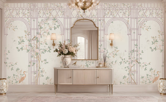 Morning Dew Trellis wallpaper in soft blush pink featuring elegant trellis arches, delicate flowering branches, perched birds, butterflies, and graceful botanical details. Styled in a sophisticated entryway with a curved gold-framed mirror, floral chandelier, fluted console table, decorative ceramic vases, and warm ambient lighting, the mural creates a serene garden-inspired backdrop that blends timeless elegance with romantic luxury.