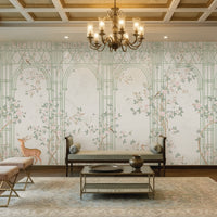 Morning Dew Trellis wallpaper in soft sage green featuring elegant trellis arches, delicate flowering vines, perched birds, graceful butterflies, and botanical details. Displayed in a sophisticated living room with a coffered wood ceiling, ornate chandelier, plush seating, brass accents, and warm wood flooring, the mural creates a serene garden-inspired backdrop that blends timeless elegance with luxurious interior design.