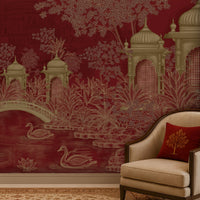 A styled interior scene featuring a deep red wallpaper with a chinoiserie-style garden pattern of pavements, a bridge, lotus flowers, and swans, paired with a cream upholstered armchair and a red decorative pillow.