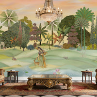 A panoramic Pichwai wallpaper mural featuring a divine Vrindavan Garden scene with hand-painted peacocks, spotted deer, and traditional figures. The design showcases lush tropical trees and a sunset-hued sky, bringing a royal Indian heritage aesthetic to a luxury living room.