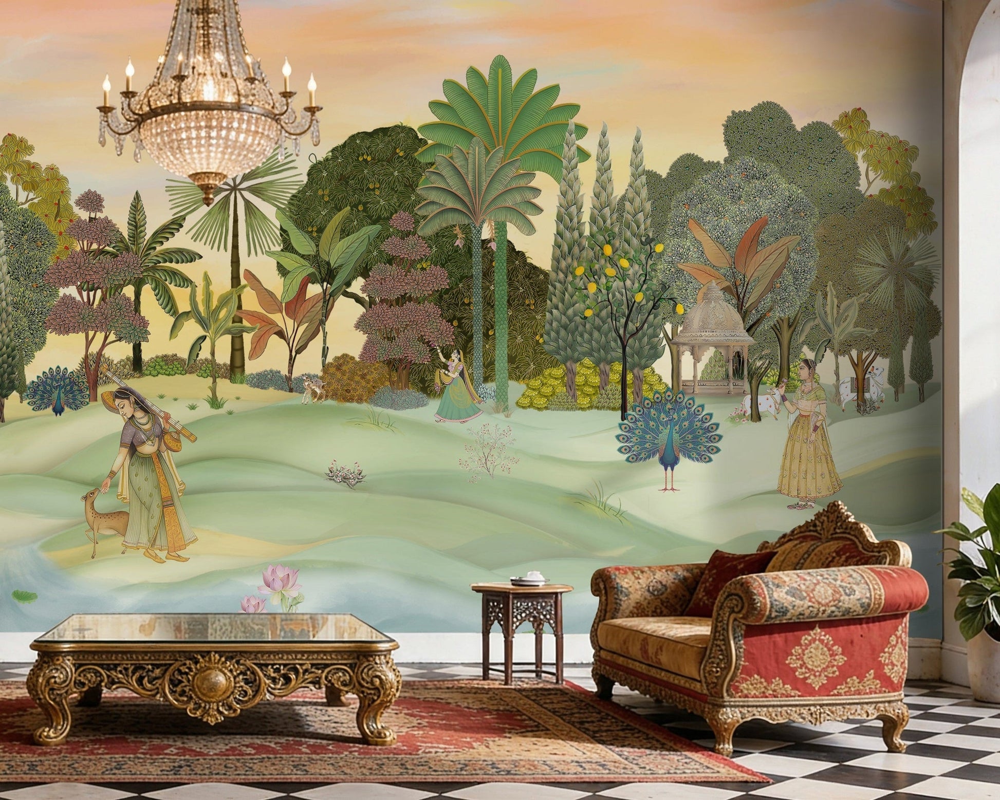 A panoramic Pichwai wallpaper mural featuring a divine Vrindavan Garden scene with hand-painted peacocks, spotted deer, and traditional figures. The design showcases lush tropical trees and a sunset-hued sky, bringing a royal Indian heritage aesthetic to a luxury living room.