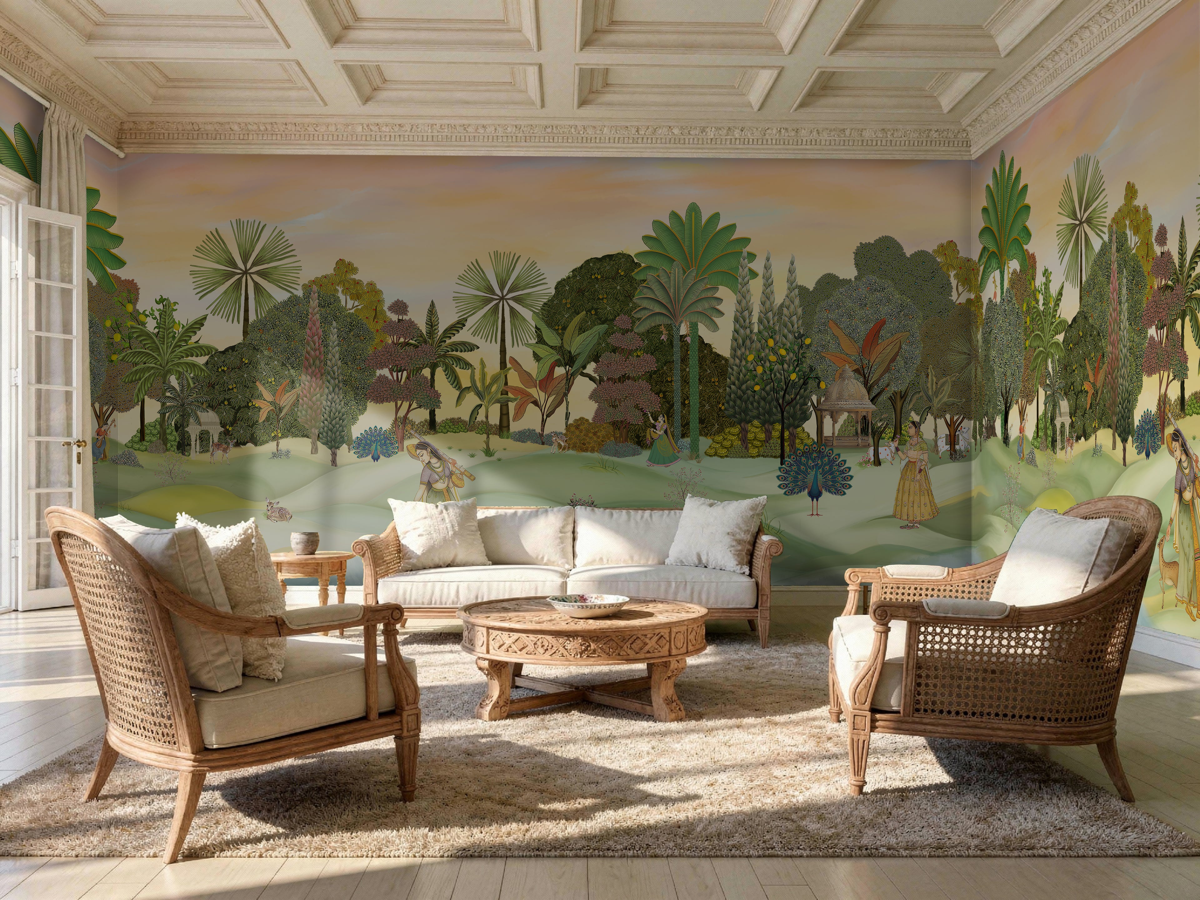 A panoramic Pichwai wallpaper mural featuring a divine Vrindavan Garden scene with hand-painted peacocks, spotted deer, and traditional figures. The design showcases lush tropical trees and a sunset-hued sky, bringing a royal Indian heritage aesthetic to a luxury living room.