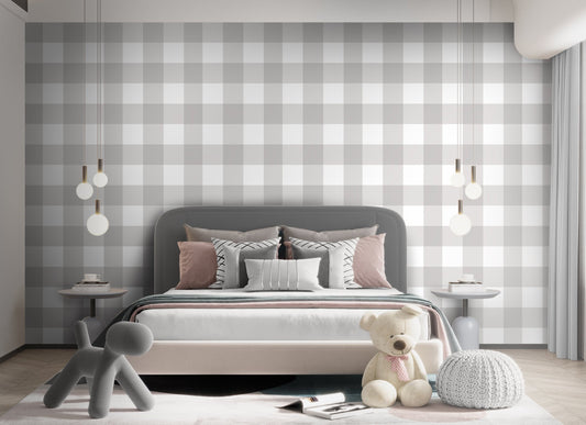 A serene nursery room features a soft gingham check wallpaper in cloud grey.
The design displays a large grid pattern with alternating light grey and white blocks.
In front, a white wooden baby crib filled with plush star and animal toys is centered.
The calm and peaceful interior layout is nicely completed by a light grey rug on the floor.