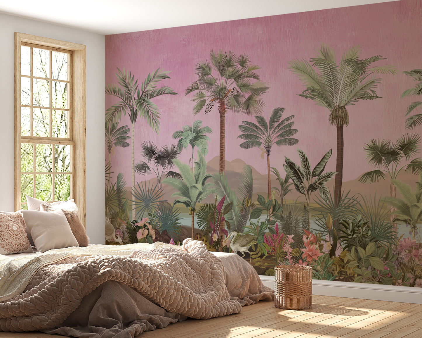 A bohemian-style bedroom featuring a large wall mural of a tropical jungle landscape with green palm trees and botanical plants against a textured pink background, paired with a chunky knit blanket and natural wood window frame.