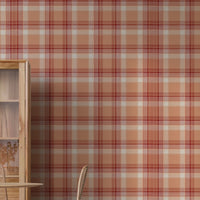 A modern dining area featuring a vibrant cinnamon-blush orange and red plaid wallpaper. On the left stands a tall, light wood display cabinet with glass doors, next to a round wooden dining table with a fluted pedestal base. Woven rattan dining chairs with slim black metal legs are arranged around the table, and a white vase filled with eucalyptus branches rests on top. The room features light-colored vertical wood plank flooring.