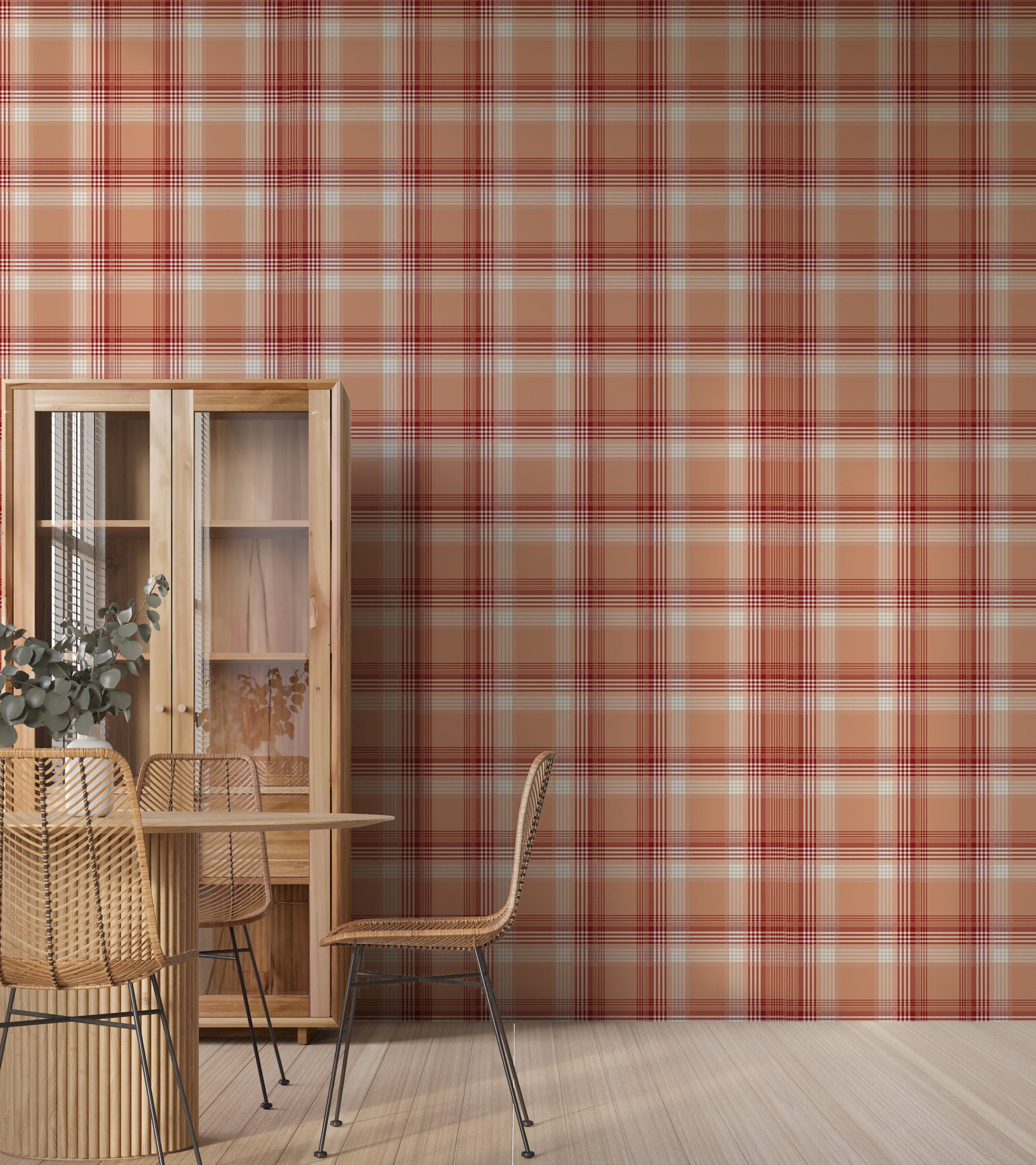 A modern dining area featuring a vibrant cinnamon-blush orange and red plaid wallpaper. On the left stands a tall, light wood display cabinet with glass doors, next to a round wooden dining table with a fluted pedestal base. Woven rattan dining chairs with slim black metal legs are arranged around the table, and a white vase filled with eucalyptus branches rests on top. The room features light-colored vertical wood plank flooring.
