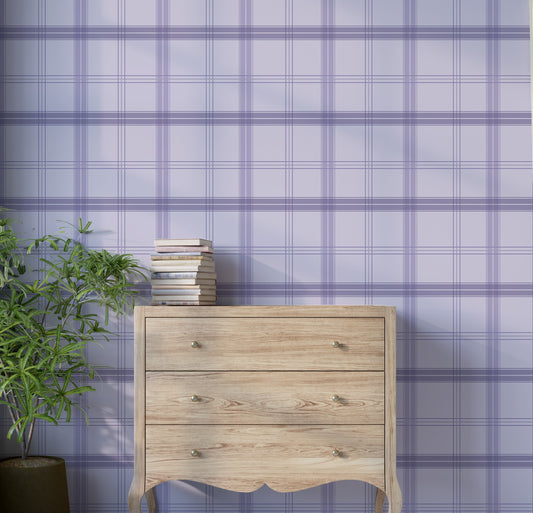A soft interior space features a classic plaid wallpaper in cloudy purple and white tones.
The textured design displays a detailed grid pattern with intersecting purple, grey, and cream lines.
In front, a minimalist light-colored wooden wishbone chair with a woven seat is centered.
The simple setting is subtly completed by a small round side table holding a dark grey vase.