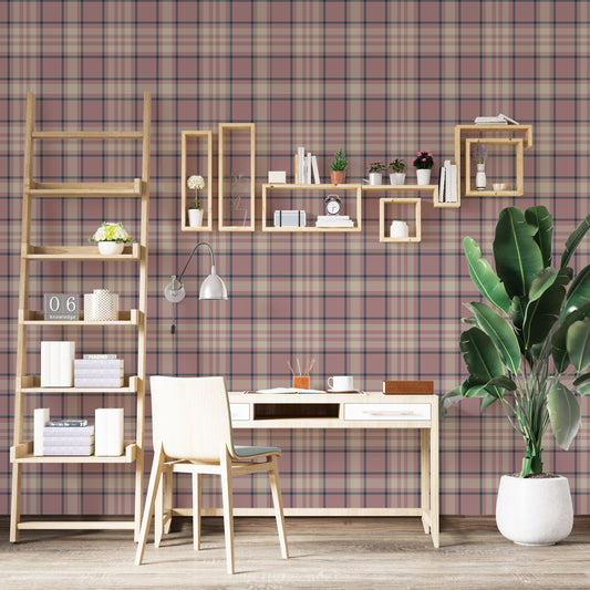 A modern living space featuring a warm desert-blush pink and white plaid wallpaper accent wall. In the center, a light oak sideboard cabinet with wooden legs holds a small wooden tripod lamp, a geometric candle, and a round white ceramic vase with a single sprig of dried pampas grass. To the left, a woven basket sits on the light wood floor, filled with tall, fluffy pampas grass stalks and a draped blanket.